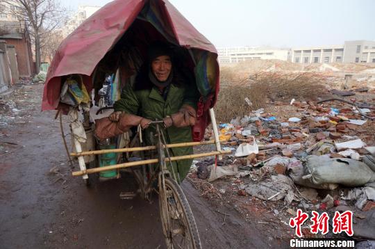 圖為老人走出窩棚，推著三輪車準(zhǔn)備出去撿拾廢品。周小云 攝