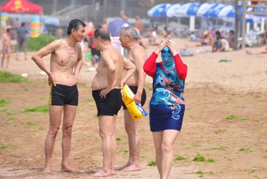 2013年7月3日，山東青島青島高溫來襲，“青島大媽”不懼滸苔，戴著“強盜面具”出現在海水浴場消暑降