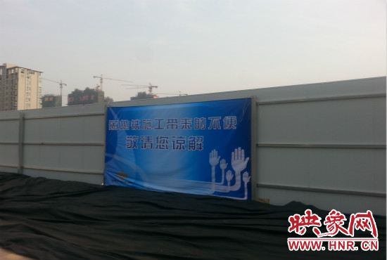 道路南側(cè)圍起了白色的圍擋，墻上標(biāo)示著“因地鐵施工帶來(lái)的不便敬請(qǐng)您諒解”的提示牌。