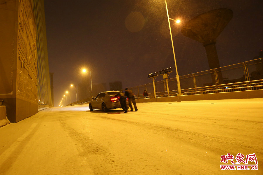 雪天路滑，汽車上橋打滑，兩名“推車人”幫助一輛私家車上坡。