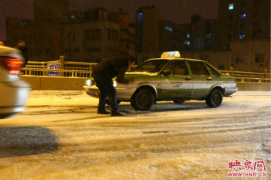 一位出租車司機在車輪前灑上雪，希望能增加輪胎的摩擦力。