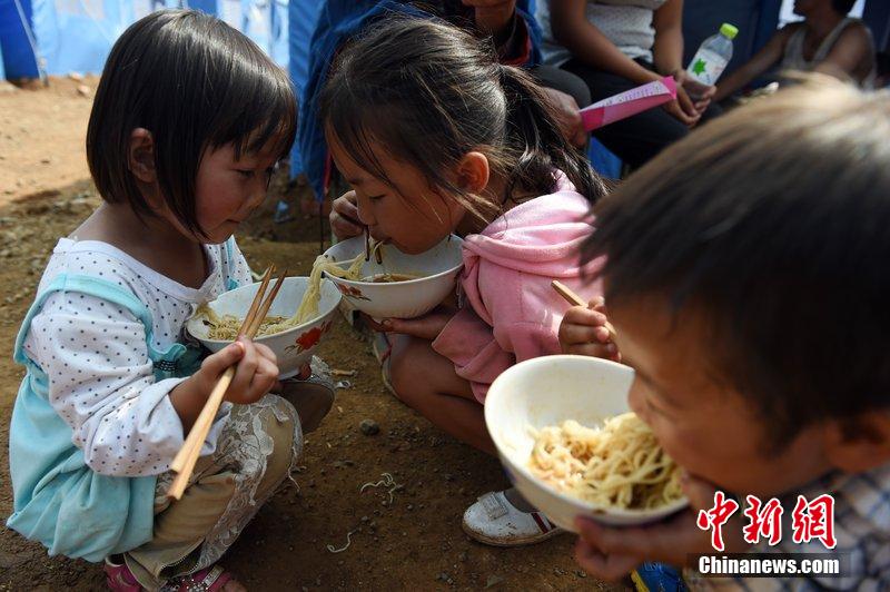 2014年8月6日，云南魯?shù)辇堫^山災(zāi)區(qū)，兒童在帳篷外吃飯。