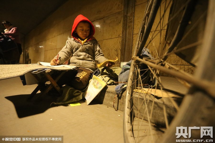 2015年11月8日晚，鄭州，7歲男孩涵洞橋下陪父母練攤，路邊燈下坐小馬扎上寫作業(yè)。