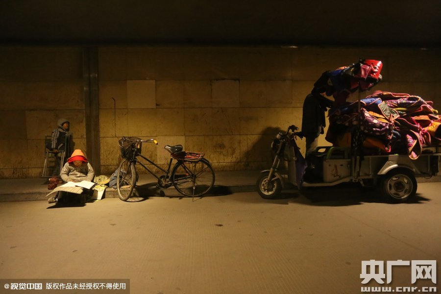 2015年11月8日晚，鄭州，7歲男孩涵洞橋下陪父母練攤，路邊燈下坐小馬扎上寫作業(yè)。